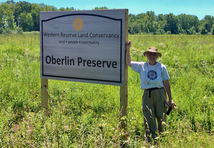 A person standing beside a sign in a prairie. The sign says 