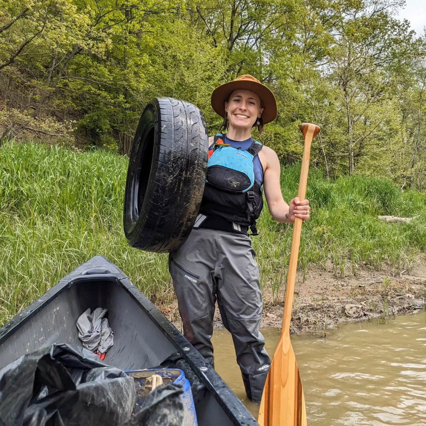 A Western Reserve Land Conservancy staff member holds up a tire pulled from the Grand River next to her canoe.